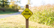 Closeup photo of a trail crossing sign with a rural scene blurred in the background