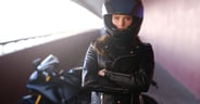Attractive serious woman is standing next to her motobike crossing hands