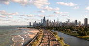 Downtown Chicago city skyline aerial centered over traffic along Lake Shore Drive between South Lagoon and Lake Michigan on a sunny day with fluffy white clouds in a blue sky above.