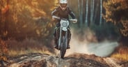 Motocross rider speeding down dirt track in forest during golden